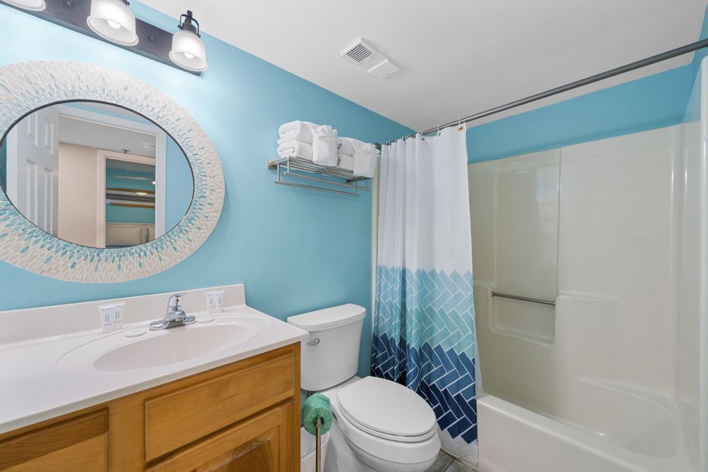 Un baño con un lavamanos blanco, un inodoro, una ducha con cortina azul y blanca, y un espejo con marco decorativo.