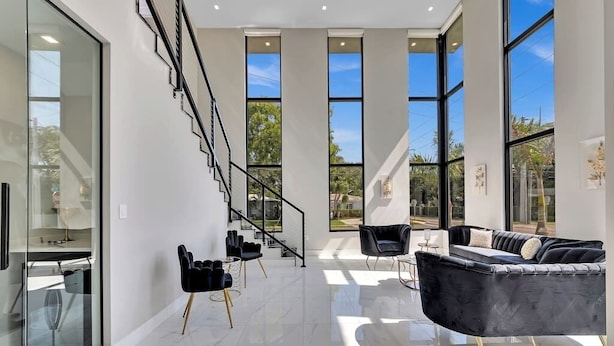 A modern interior with a staircase, black chairs, a black sofa, and large windows.