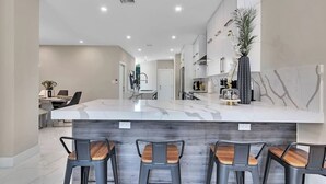 A modern kitchen with a marble island, bar stools, and a decorative plant.