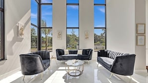 A modern living room with a black sofa set, a round coffee table, and large windows offering a view of the outdoors.