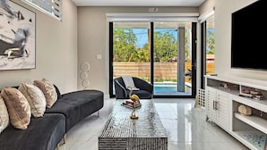 A modern living room with a sofa, coffee table, TV, and a sliding glass door leading to a pool.
