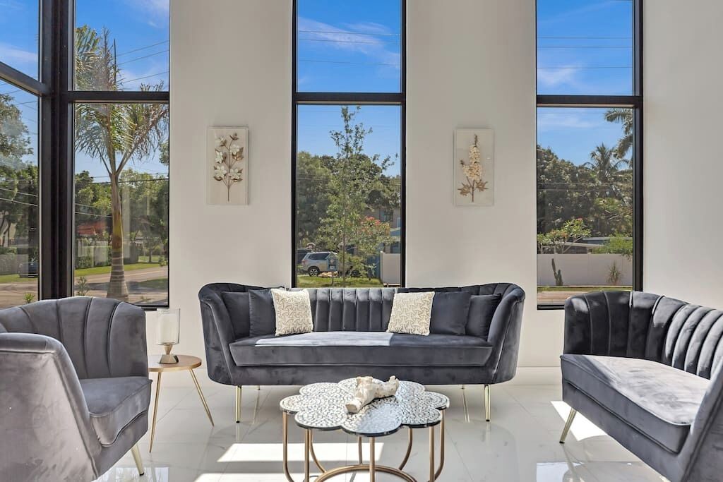 Een moderne woonkamer met een donkergrijze bank, twee fauteuils en een ronde salontafel. Grote ramen bieden uitzicht op de omgeving.