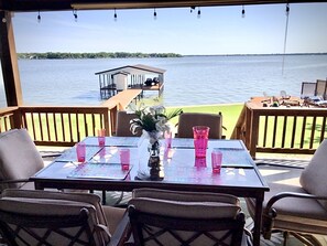 A table set for dining with chairs, overlooking a lake with a dock and a small building in the background.