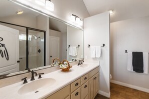 A bathroom with a large mirror, two sinks, a shower, and a towel rack.