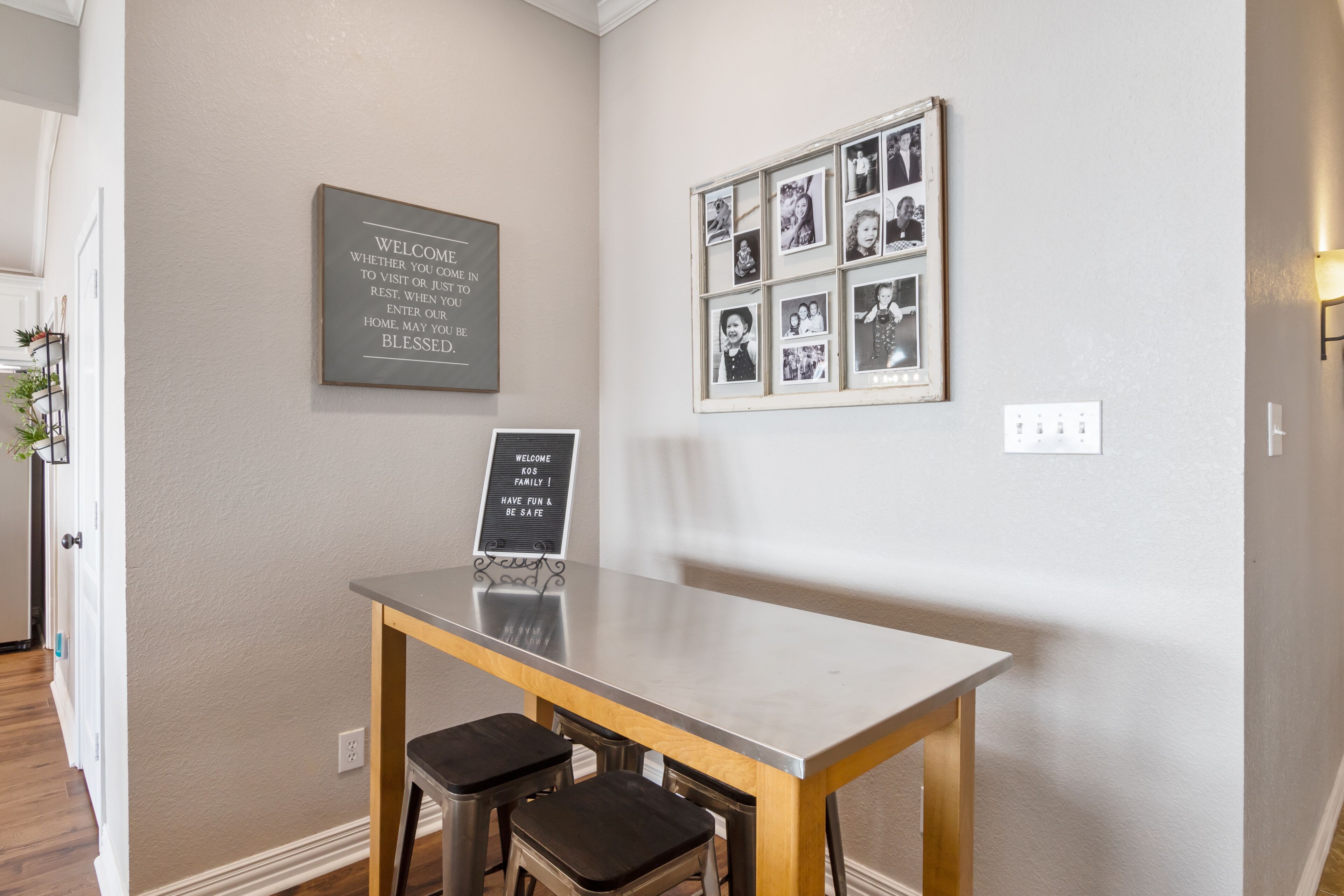 Une pièce propre et moderne, avec une table en bois et deux tabourets, un mur orné d’un collage de photos encadrées, et deux panneaux d’accueil.