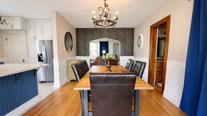 Un comedor con mesa de madera y sillas de cuero, una araña y una cocina al fondo.