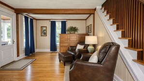 Amplia sala de estar con pisos de madera, un sofá de cuero marrón, un mueble de madera y una escalera con barandilla de madera.