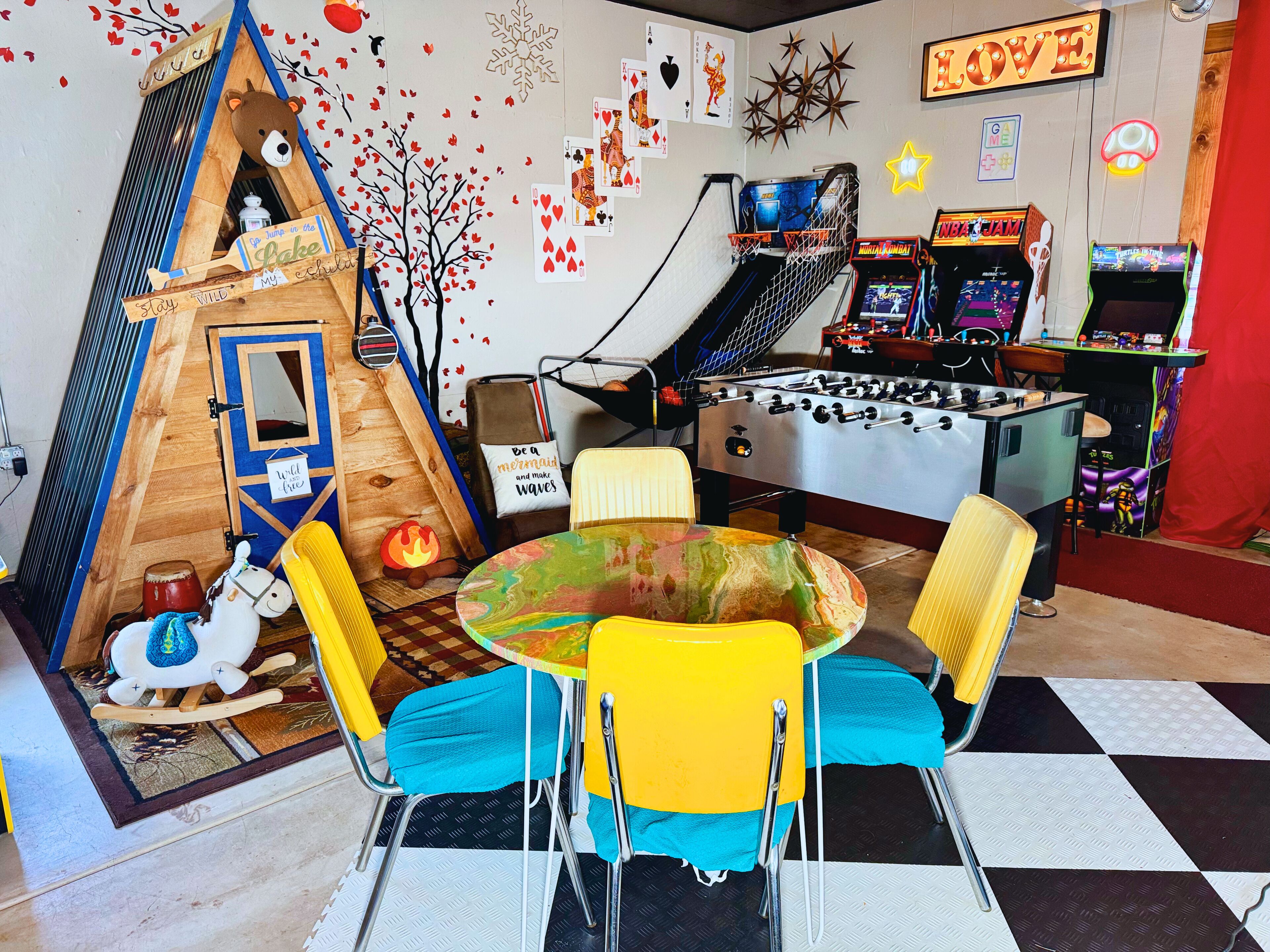 A playroom with a foosball table, a small playhouse, and a colorful table with chairs.