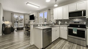 A modern kitchen with white cabinets, stainless steel appliances, and a large window. - Pet Friendly Customized Harbor Village Condo (Manistee)