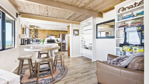 Eine moderne Küche mit Holzschränken, ein Essbereich mit Hocker und eine gemütliche Sitzecke mit einer Couch und einer Decke.