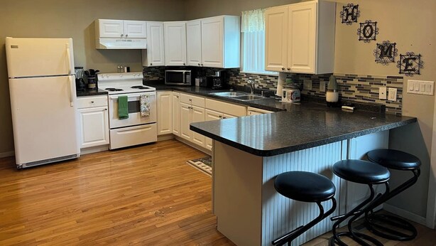 A kitchen with white cabinets, a refrigerator, a stove, a microwave, a sink, and a bar area with stools. - Wonderful two-bedroom home with a full kitchen (Pierre)