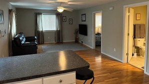 A modern living room with a black leather sofa, a granite island, and a flat-screen TV mounted on the wall. - Wonderful two-bedroom home with a full kitchen (Pierre)