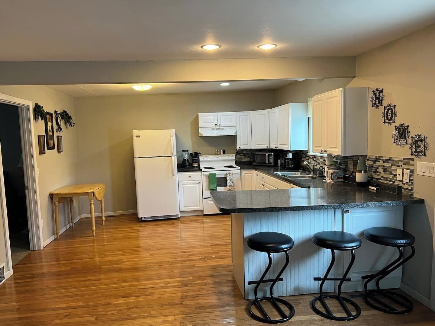 A kitchen with white cabinets, a black countertop, and three black stools.