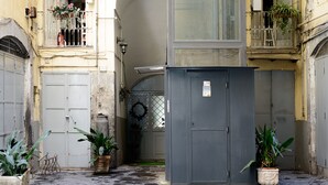 A narrow alleyway with a grey utility box, potted plants, and a metal gate. - Giardino Segreto - Via Foria 216 (Ammezzato) (Napoli)