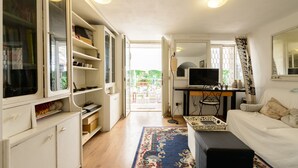 A compact living space with a sofa, a television, a desk, and a bookshelf. - Giardino Segreto - Via Foria 216 (Ammezzato) (Napoli)