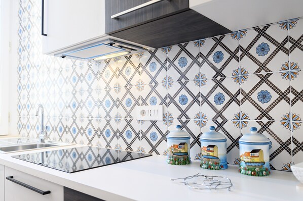 A kitchen with a modern design, featuring a patterned backsplash, a stainless steel sink, and two decorative jars on the counter.