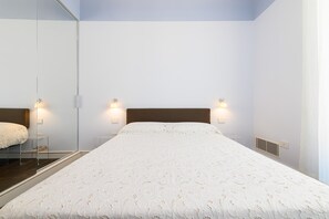 A bedroom with a large bed, a mirror, and wall-mounted lights.