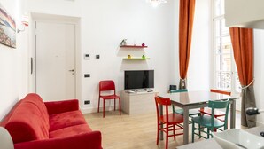 Un espace de vie compact comprenant un canapé rouge, une table à manger avec des chaises, un téléviseur et une fenêtre avec des rideaux.