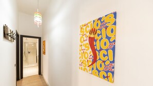 Un couloir agrémenté d’un luminaire moderne, d’une porte de douche en verre et d’une œuvre d’art aux couleurs vives accrochée au mur.