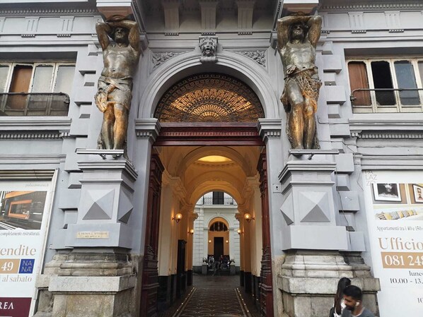 Uma entrada imponente com duas estátuas de cada lado, um arco ornamentado e uma placa para um escritório comercial.