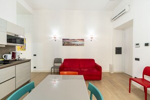 A compact living space with a kitchenette, a dining table, a red sofa, and a painting on the wall.