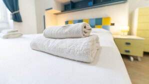 Siististi pedattu sänky, jonka päällä on taiteltu valkoinen pyyhe, yöpöytä, jossa on lamppu, ja sinivalkoruudullinen seinä.
