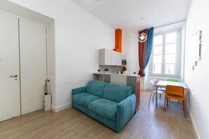 Un salon moderne avec un canapé de couleur turquoise, un petit coin cuisine et une table à manger avec des chaises.