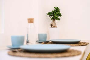 Une table à manger avec une plante en pot, deux tasses bleues et une bouteille.