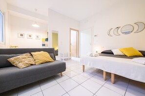 Una habitación moderna con un sofá gris, una cama con ropa de cama blanca y una mesita pequeña blanca.