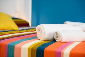 Un letto con una coperta a righe colorate e un asciugamano bianco arrotolato sopra.
