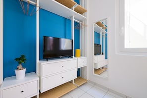 Un bagno moderno con una parete blu, mobili bianchi, una TV a schermo piatto, una pianta in vaso e uno specchio.
