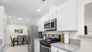 Une cuisine moderne avec des meubles blancs, un réfrigérateur en acier inoxydable, un four à micro-ondes, une cuisinière et un coin repas comprenant une table et des chaises.