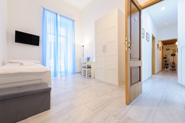 A modern hotel room with a bed, a desk, a wardrobe, and a television.
