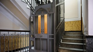 Una reixa de metall amb un disseny decoratiu, una escala amb barana i un paviment de marbre.