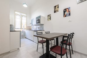 A compact kitchen with a dining area, white cabinets, a microwave, and a window.