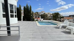 A rooftop pool area with tiled flooring, white lounge chairs, and a view of surrounding buildings. - VILLA NEILA, with heated pool  (URBANIZACIÓN PUERTO AZUL, TARAJALEJO)