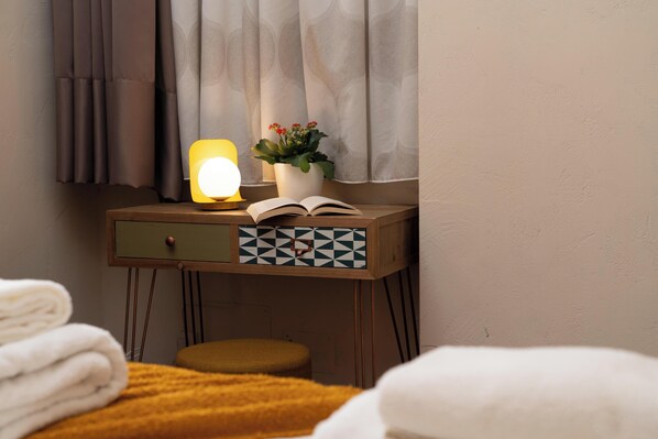 A bedside table with a lamp, an open book, a potted plant, and a folded towel.