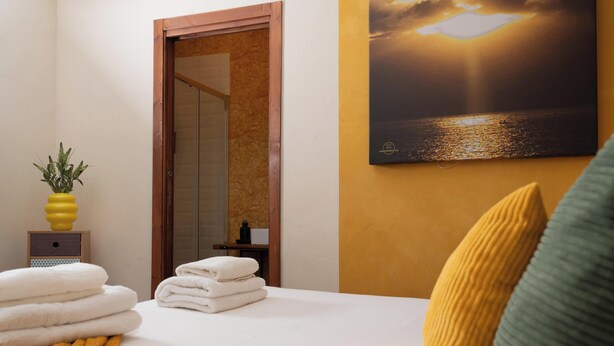 A hotel room with a bed, a painting of a sunset, a small plant, and a wooden door. - Napolicentrico - Three Bedroom Apartment, Sleeps 8 (Napoli)