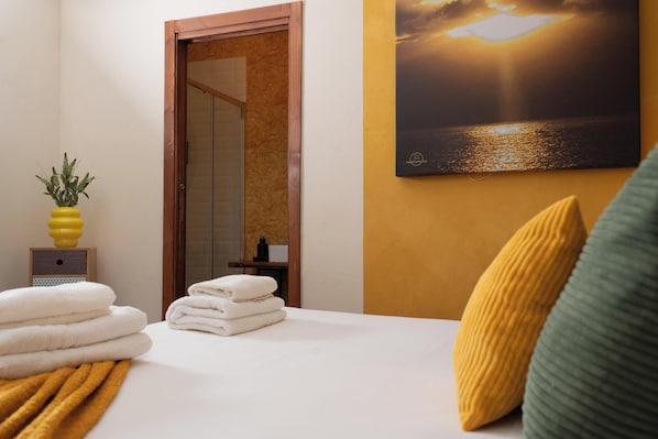 A hotel room with a bed, a painting of a sunset, a small plant, and a wooden door.