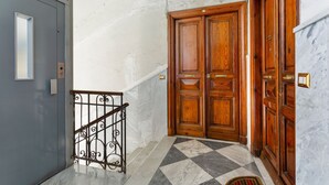 Un couloir avec un sol à carreaux, une porte grise et des portes doubles en bois.