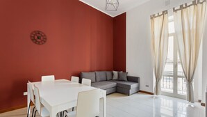Une pièce spacieuse comprenant une table à manger, des chaises, un canapé gris et une grande fenêtre avec des rideaux.