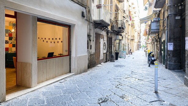 A narrow cobblestone street with a shop on the left and parked motorcycles on the right. - Via S. Liborio 79 - 6° Piano (Napoli)