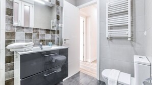 A modern bathroom with a large mirror, a black vanity, a toilet, and a white towel rack.