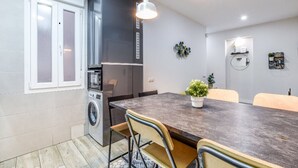 A modern kitchen with a built-in washing machine, a large dining table, and pendant lights.