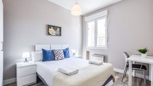 A modern bedroom with a large bed, bedside tables, a desk, and a window.