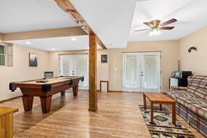 A spacious room with a pool table, a sofa, a ceiling fan, and a door leading to an outdoor area.