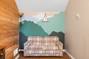 A room with a plaid sofa, wooden panel walls, a mountain mural, and a hanging decoration.