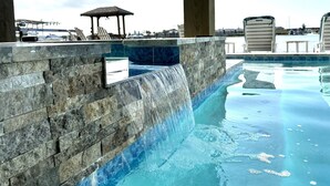 A swimming pool with a waterfall feature, stone walls, and lounge chairs.