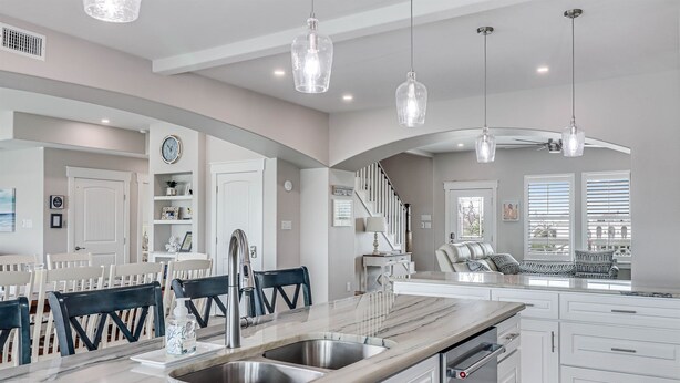A modern kitchen with a marble countertop, stainless steel sink, and pendant lights.