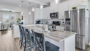 A modern kitchen with white cabinets, stainless steel appliances, and a marble island with bar stools.
